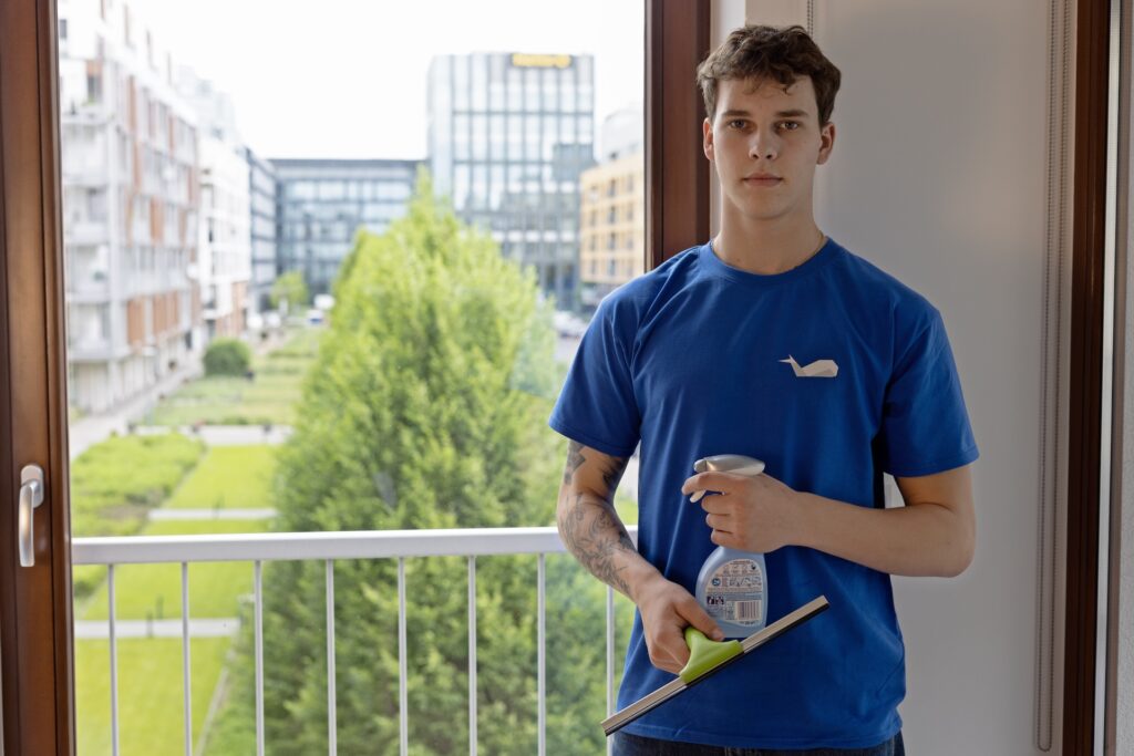 Pracownik firmy sprzątającej myje okna w mieszkaniu z widokiem na nowoczesne osiedle